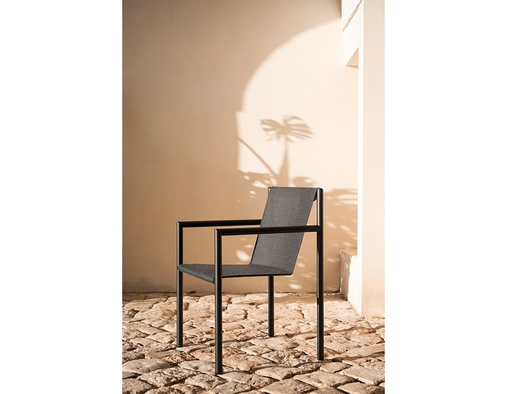 Minimalist outdoor chair with a matte black frame and dark grey fabric seat. Set against a sunlit stone patio with soft shadows, it brings refined style and modern comfort to outdoor spaces.