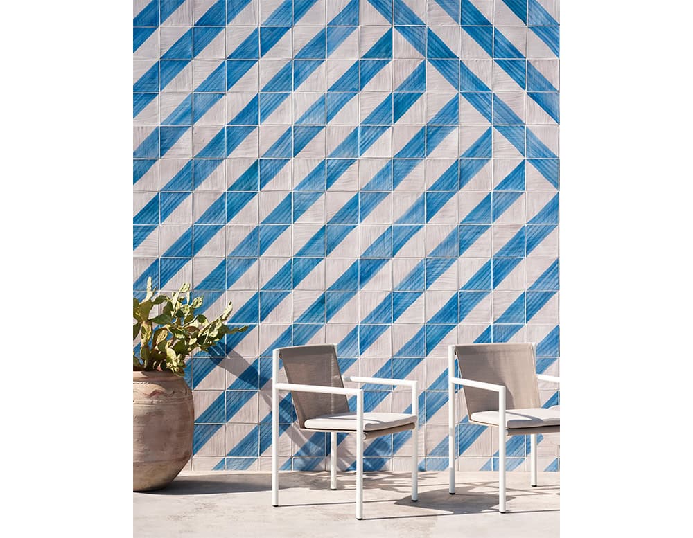 Outdoor chairs with crisp white frames and taupe mesh seats, arranged beside a vibrant blue geometric tile wall. Their sleek lines and airy materials offer a light, modern touch perfect for sunny patios or poolside lounges.