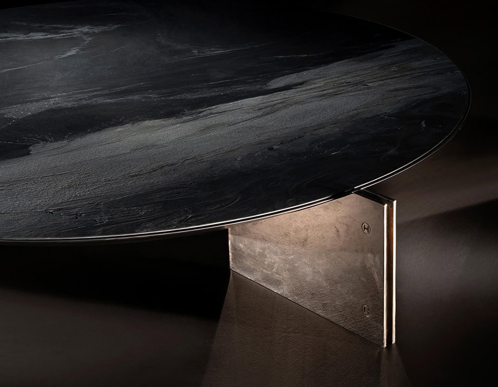 The Muse Coffee Table features a dark veined stone top and a patinated metal leg, combining refined materials with sculptural presence in a compact, elegant design.