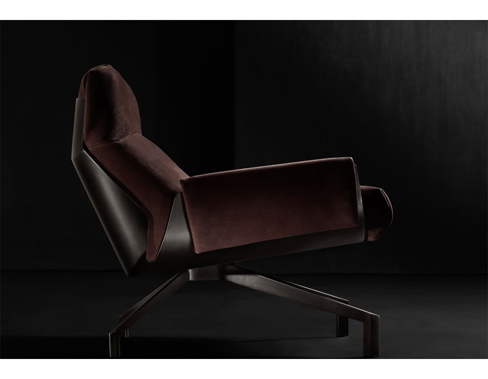 The Hen Club 57 Armchair is shown in profile, revealing its ergonomic tilt and rich burgundy upholstery. A sleek dark frame and angled metal base enhance its modern, sculptural silhouette against the black background.