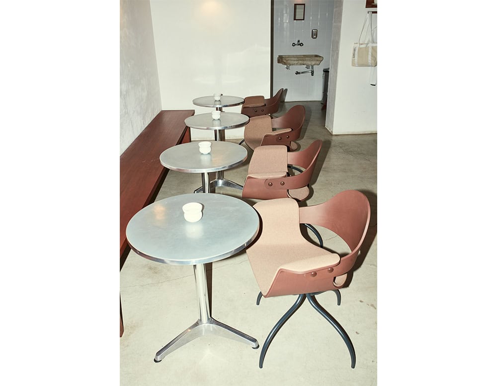 Showtime Bar Chair shown in a soft clay hue, offering a distinctive silhouette with a sculpted shell and exposed fasteners. The combination of curved plywood and graceful metal legs brings both poise and personality to cafe settings.