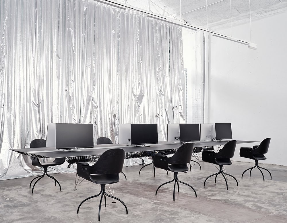 Showtime Bar Chair in a deep ebony tone, shown in a sleek workspace setting. Its bold curvature and industrial leg structure contrast with the refined workstation setup, offering a sculptural approach to task seating.