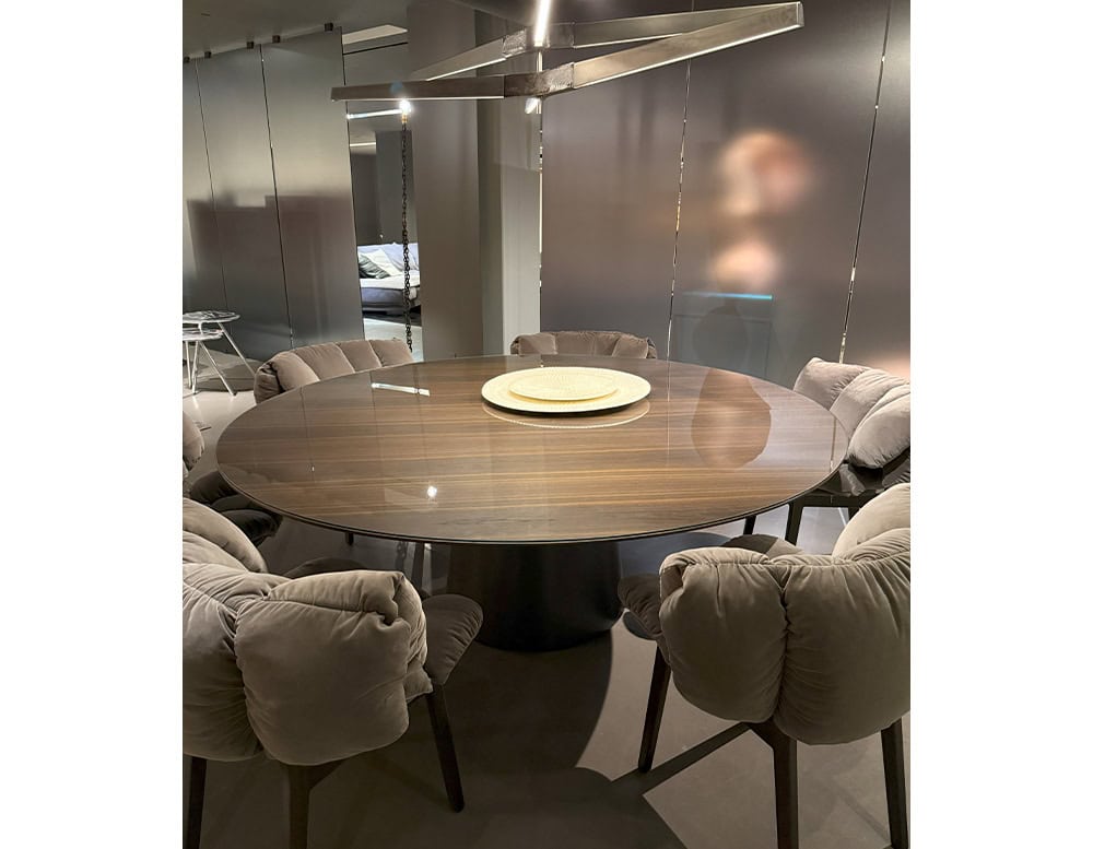 The Emmemobili UFO Dining Table features a round wood veneer top with a glossy finish and central pedestal base. It is paired with tufted grey chairs, creating a warm, inviting dining setting with soft lighting and contemporary accents.