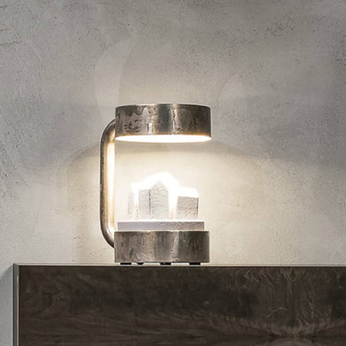 Compaud Table Lamp merges rough-textured metal with polished geometric crystals. The piece provides ambient light while showcasing sculptural elegance, ideal for minimalist or contemporary settings.