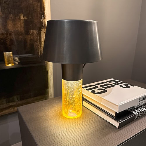 Ghost Table Lamp D25 offers a striking balance of matte black and warm amber glass. Its bold form and radiant glow bring visual interest to shelves or nightstands, enhancing modern interiors with its sculptural and luminous appeal.