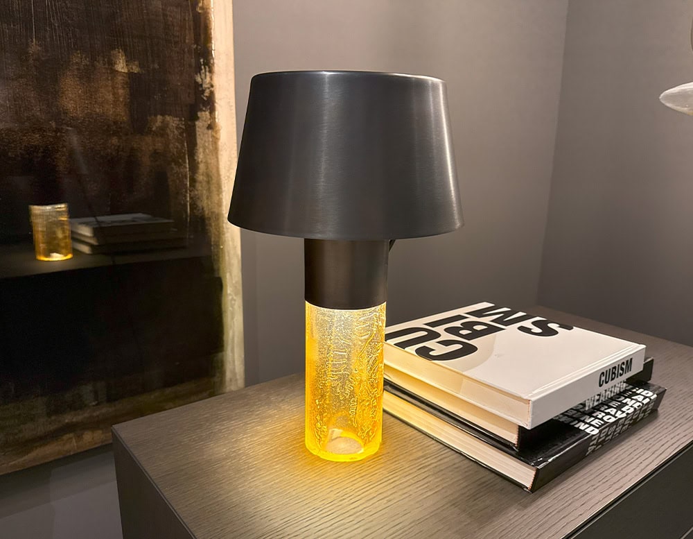 Ghost Table Lamp D25 features a glowing amber glass base paired with a matte black aluminum shade. This compact yet striking design offers soft, diffused light and adds a warm, sculptural accent to side tables or nightstands.