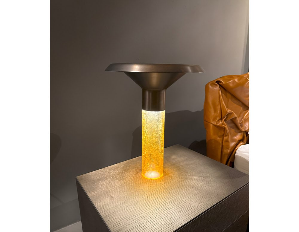 Ghost Table Lamp D38 pairs a translucent amber-glow cylinder with a dark flared top, offering both visual warmth and sculptural appeal. The light softly diffuses through the base, enhancing modern interiors with subtle luminosity.