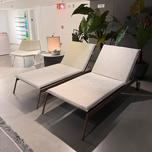 Refined loungers with bronze frames and light beige cushions, set against lush foliage and soft lighting. This inviting composition offers a serene blend of modern elegance and natural relaxation.