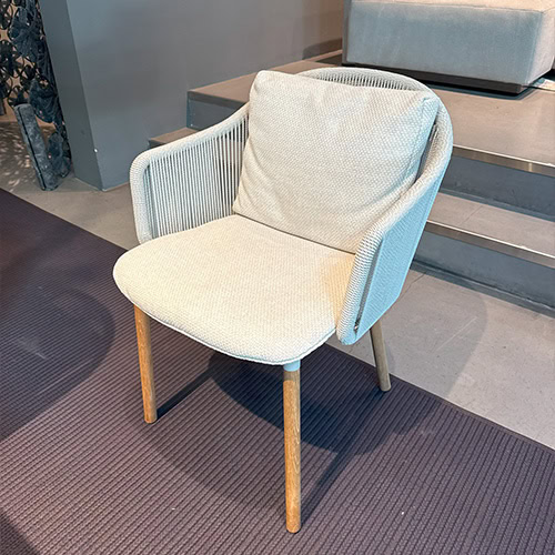 The Tri Senja Outdoor Dining Chair features a refined silhouette with gently curved rope arms and plush seating. Its tactile fabric and warm wooden legs create a modern relaxed look suited for versatile outdoor settings.