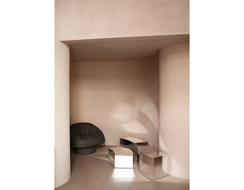 A set of reflective stainless steel coffee tables arranged within a softly curved architectural alcove, creating a harmonious dialogue between geometry, material, and space.