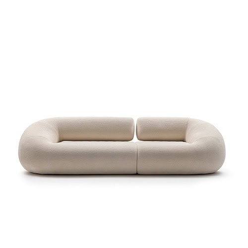 A sculptural Evolis Next Sofa in a pale tone, featuring low rounded backrests and generous seat proportions. The modular design creates a soft and continuous seating landscape, inviting relaxation.