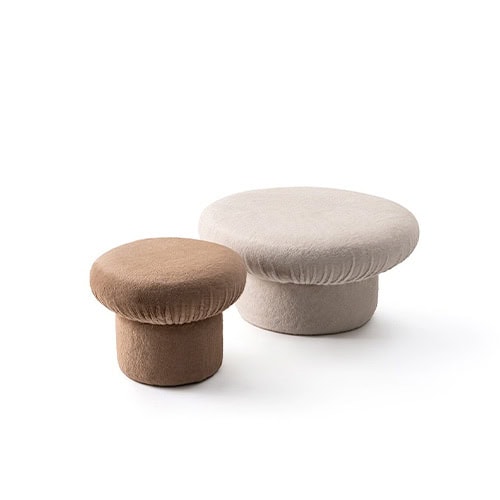 The GR Nala Stools are presented in a clean setting. One is soft beige, the other warm taupe, both with plush rounded forms and cylindrical bases, evoking cozy and sculptural appeal.