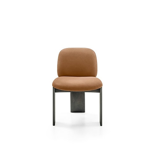 The GR Saki Chair presents a compact silhouette with a softly curved backrest and seat, upholstered in warm, earthy fabric. Its slender legs frame a central wood support, blending comfort with minimalist structure.