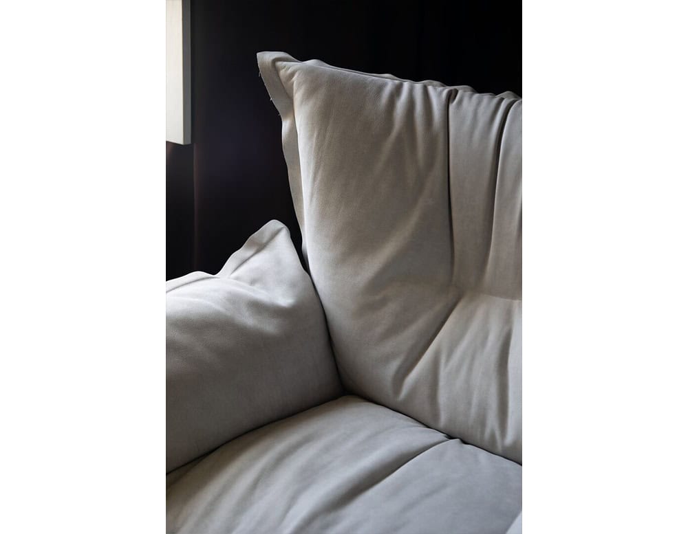 Close up of the armchair in soft grey upholstery highlighting its generously padded cushions and elegant stitching for a cozy and refined look.