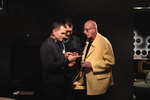 Guests pause to share a moment over a phone, their conversation unfolding against the warm ambiance of the showroom where refined lighting and contemporary pieces set the tone for a relaxed evening.