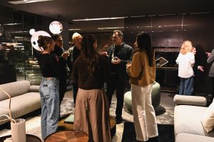 A relaxed moment on the showroom floor as guests gather in small circles, drinks in hand, chatting and discovering the designs around them.