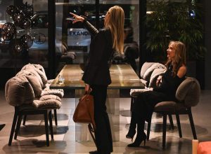 Conversation flows effortlessly as two guests take in the showroom’s refined setting, one pointing out a detail while the other enjoys the moment in a beautifully lit and stylish space.