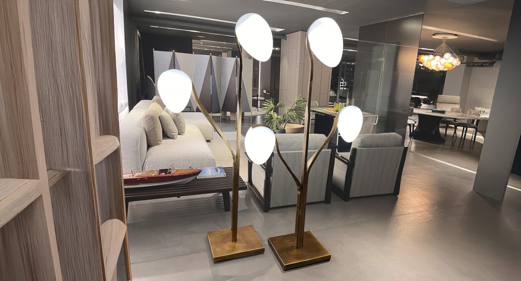 Sculptural floor light with branching bronze stems and softly glowing white glass forms. Inspired by organic shapes, it brings a warm ambient presence, pairing golden metal tones with diffused light in a refined interior setting.