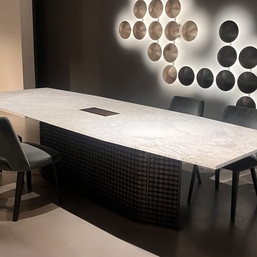 S Penny dining table with a light marble top featuring subtle gray veining, paired with a sculptural dark wood base. Shown with deep charcoal upholstered chairs, the palette blends soft stone tones with rich wood and dark accents.