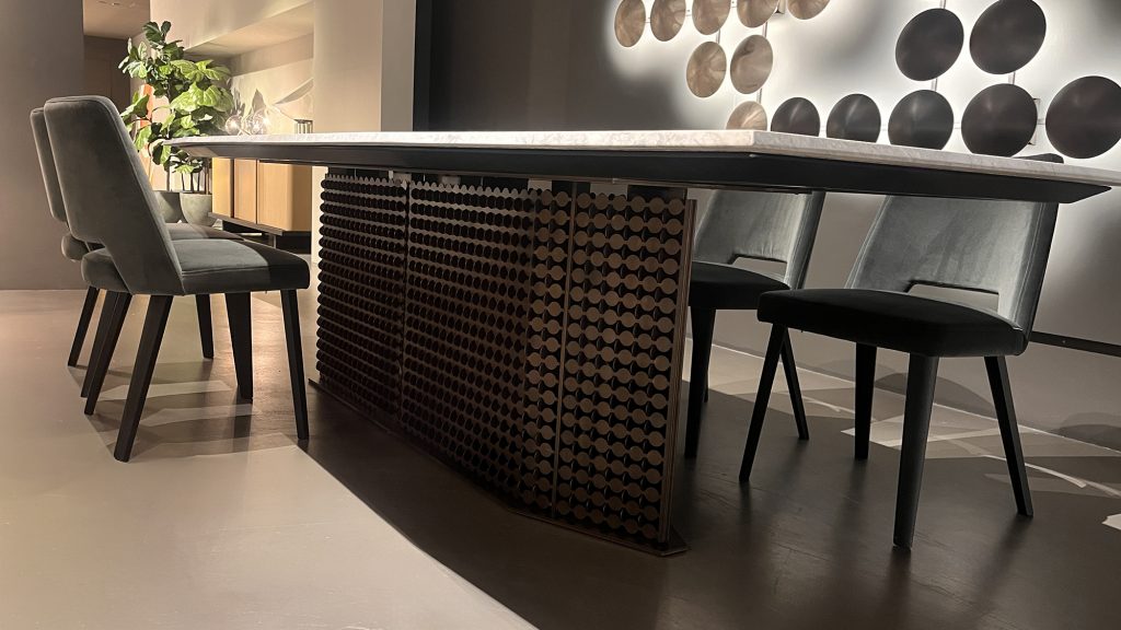S Penny dining table showcasing a pale marble top with soft gray veining set over a sculptural dark wood base with geometric detailing, paired with charcoal upholstered chairs for a rich contrast of light stone, deep wood, and muted gray tones.