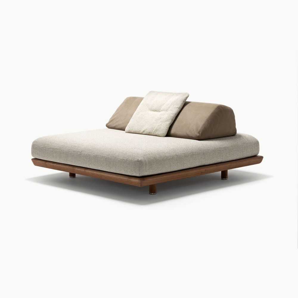 Caprera island sofa module with a wide cushioned seat in soft natural beige fabric paired with warm taupe and light cream back cushions resting on a low dark wood base creating a relaxed versatile lounge piece.