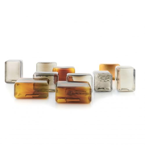 A collection of sculptural glass tables in warm amber and soft neutral tones creates a dynamic, light-filled arrangement. Their rounded forms and translucent finishes bring depth, reflection, and a subtle sense of movement to the space.