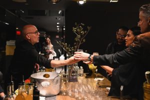 A bartender serves cocktails as guests connect across the bar, capturing the warm hospitality and refined atmosphere of the evening event.