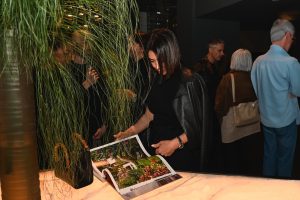 A guest browses a beautifully styled design book during the evening event, surrounded by lush greenery and a refined, intimate showroom atmosphere.