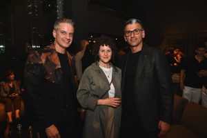 Three guests pose together at a stylish evening gathering, showcasing modern tailoring, relaxed elegance, and a warm, intimate event atmosphere.