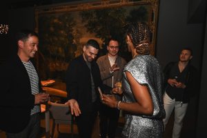 Guests engage in lively conversation beside a dramatic mural backdrop, blending contemporary style, warm hospitality, and an intimate evening ambiance.