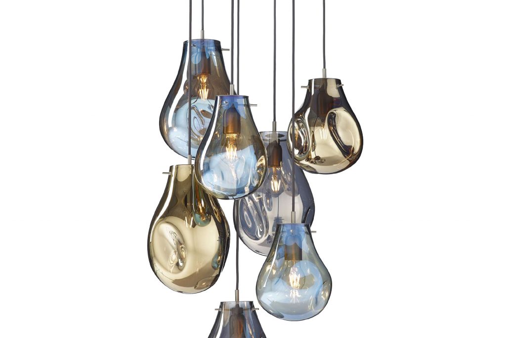 A cluster of hand blown glass pendant lights in soft blue and warm amber tones hangs at varying heights. Their rounded organic shapes and transparent finish create depth, while the exposed bulbs add a warm glow to the sculptural composition.