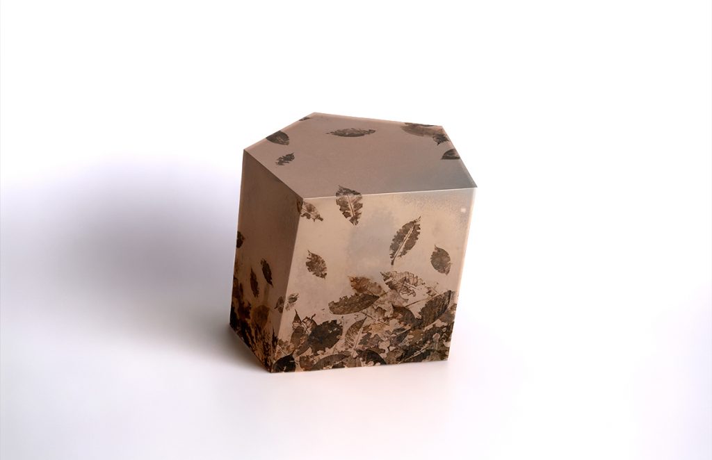 This side table features a faceted pentagonal form crafted from translucent resin with preserved leaves embedded throughout. Botanical details and layered textures create depth, bringing an organic character to its sculptural contemporary silhouette.