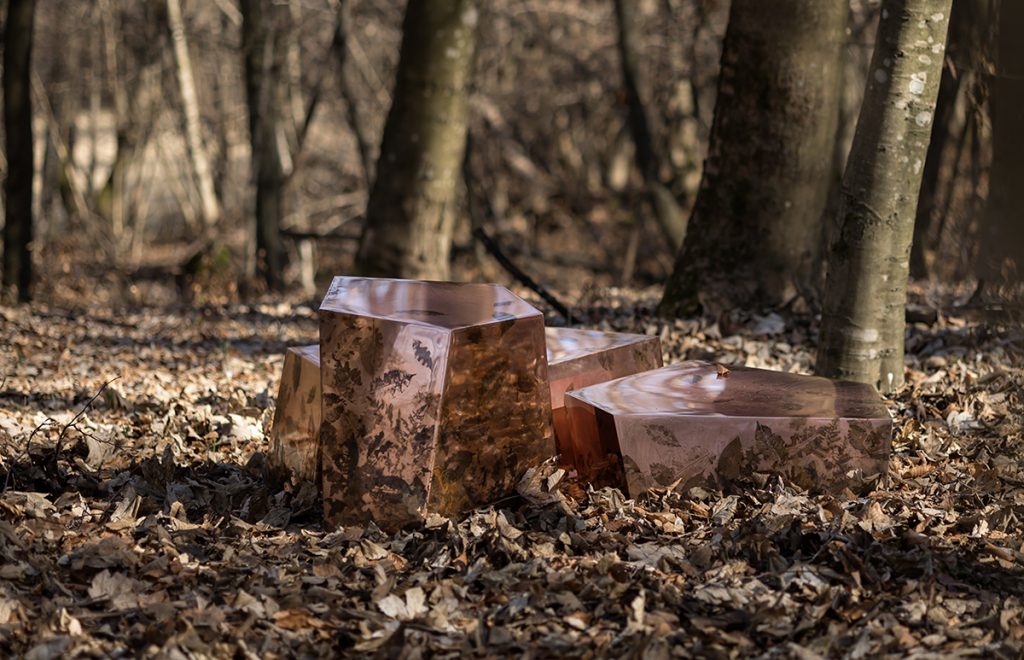 Shown in a natural setting, these side tables feature faceted resin forms with preserved leaves and botanical fragments. Their sculptural silhouettes and organic textures echo the surrounding landscape, reinforcing a connection to nature.