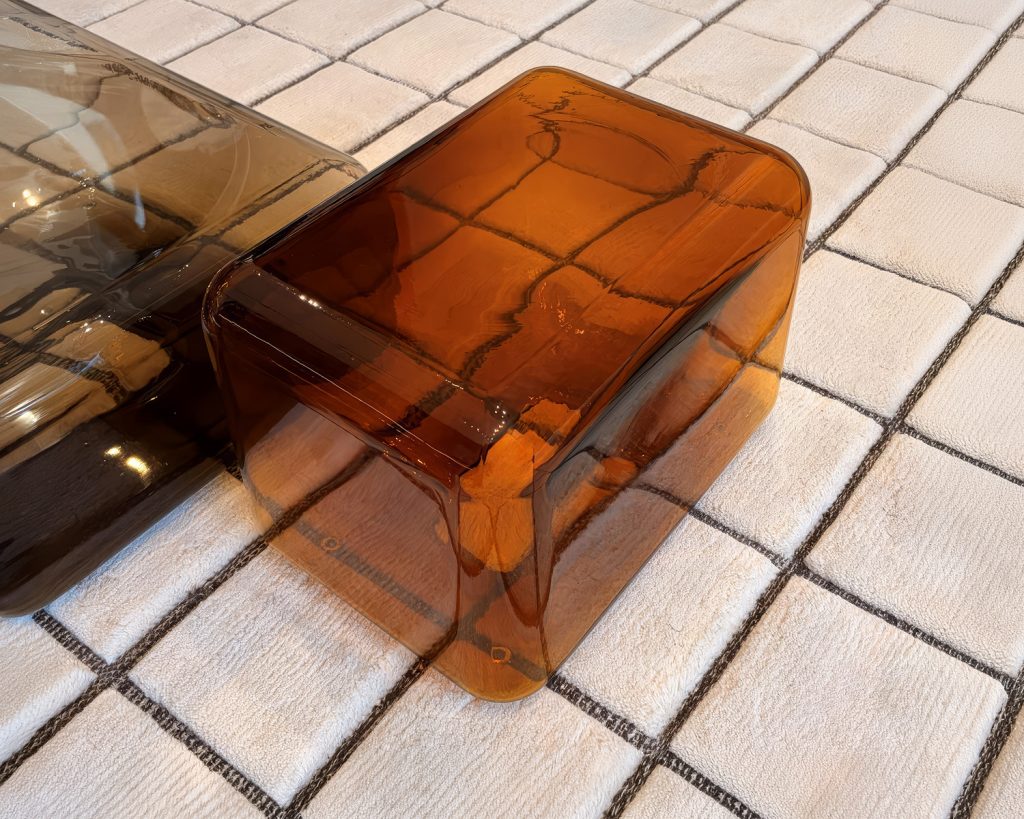 A low coffee table in translucent amber glass features softly rounded edges and a seamless sculptural form. Its warm tone and glossy surface catch the light, creating subtle reflections that enhance its refined contemporary design.