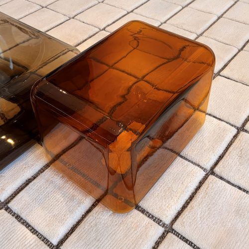 A low coffee table in translucent amber glass features softly rounded edges and a seamless sculptural form. Its warm tone and glossy surface catch the light, creating subtle reflections that enhance its refined contemporary design.